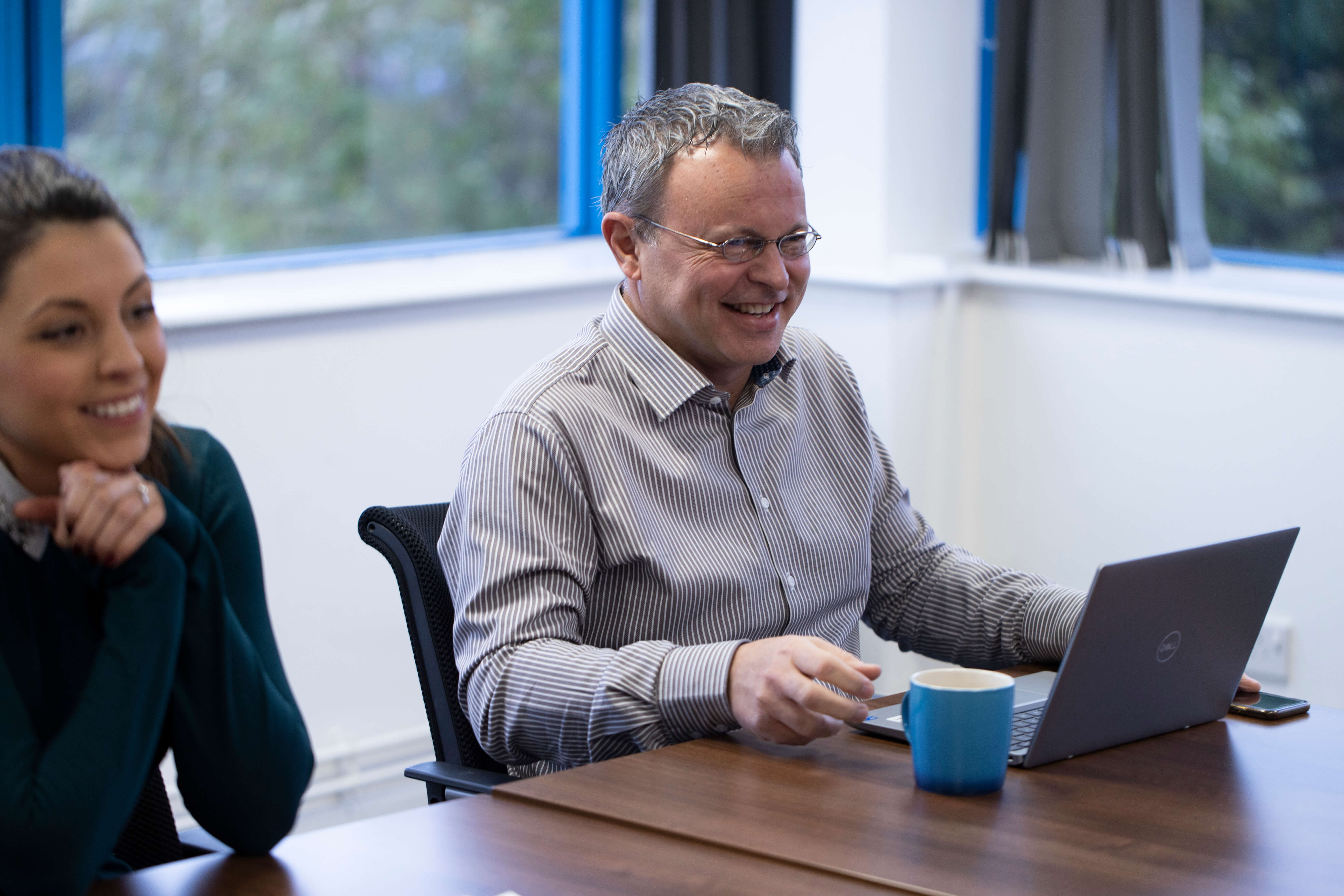 A man smiling sat a laptop with a mug of a hot drink with him
