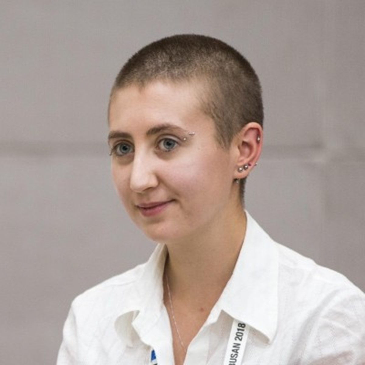 A close-up of a woman in a white shirt smiling against a beige backdrop