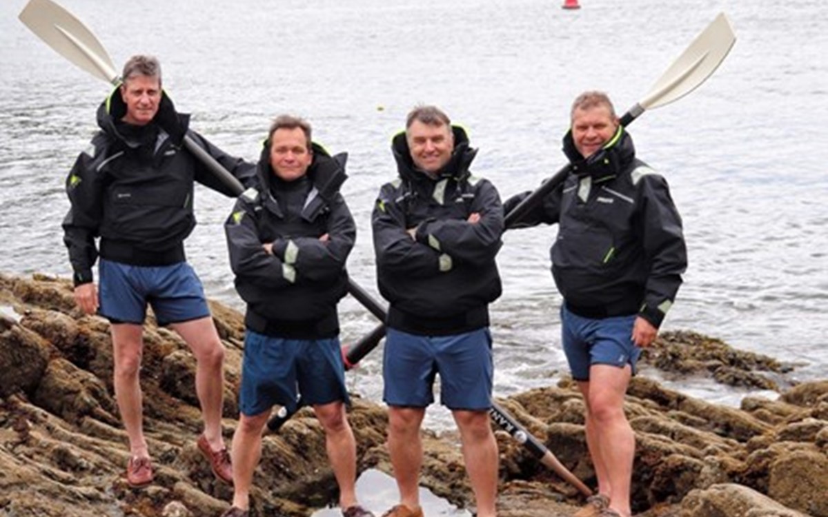 A group of people stand on some rocks holding paddles with the sea in the background