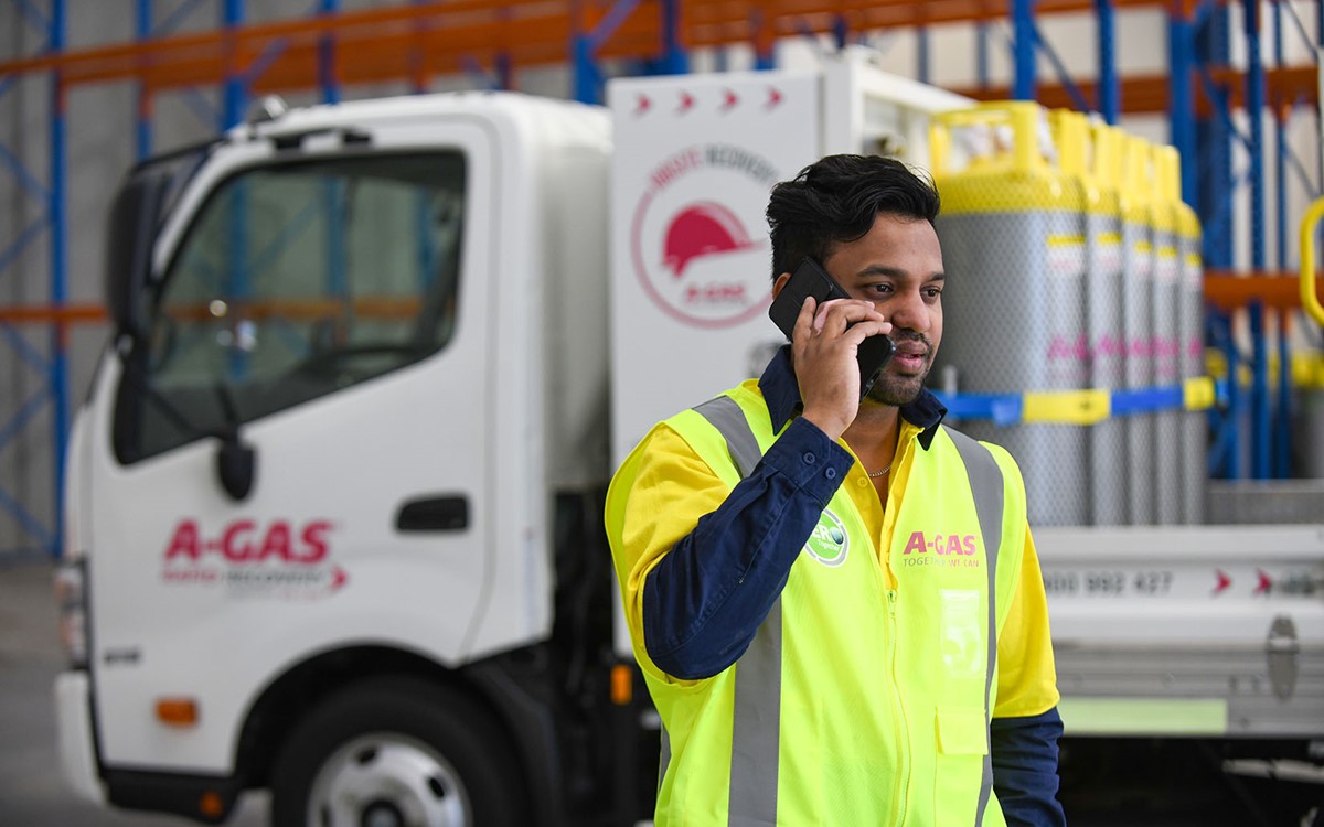 A man in a yellow high-vis jacket talking on the phone in front of a white A-Gas truck