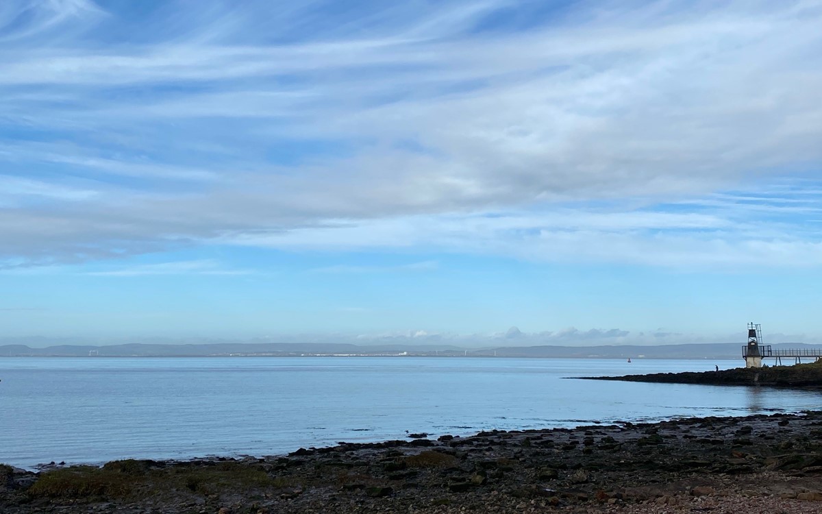 A wide shot of a beach and bay area with a lighthouse on the right-hand side