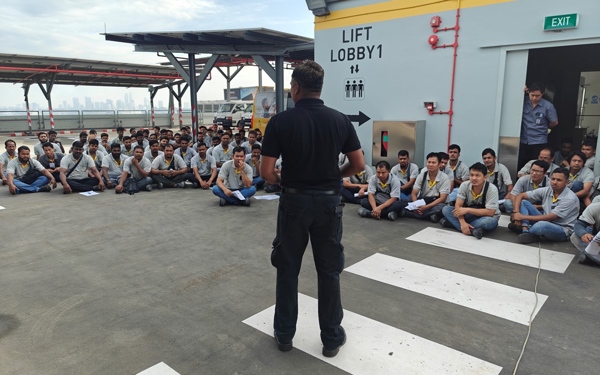 A man speaks to a group of people sitting down outside