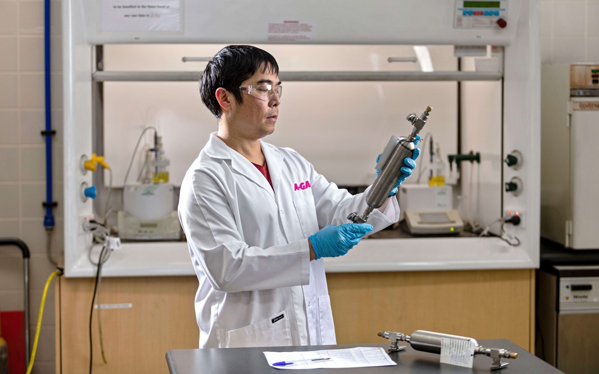 Technician in a white coat working holding a silver metal tool in a laboratory