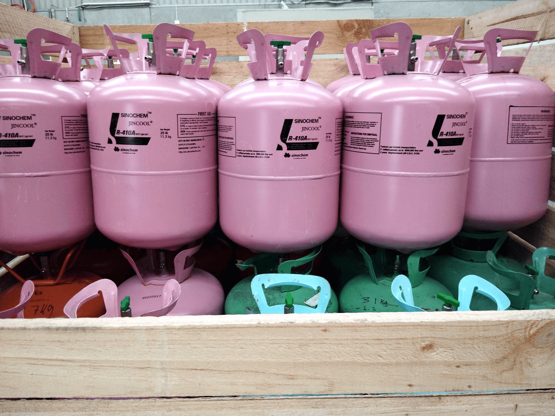 Rows of pink disposable cylinders on top of green, pink and red cylinders in a wooden crate 