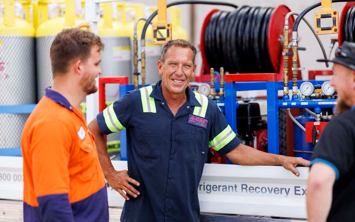 Three men talking and smiling next to a Recovery truck