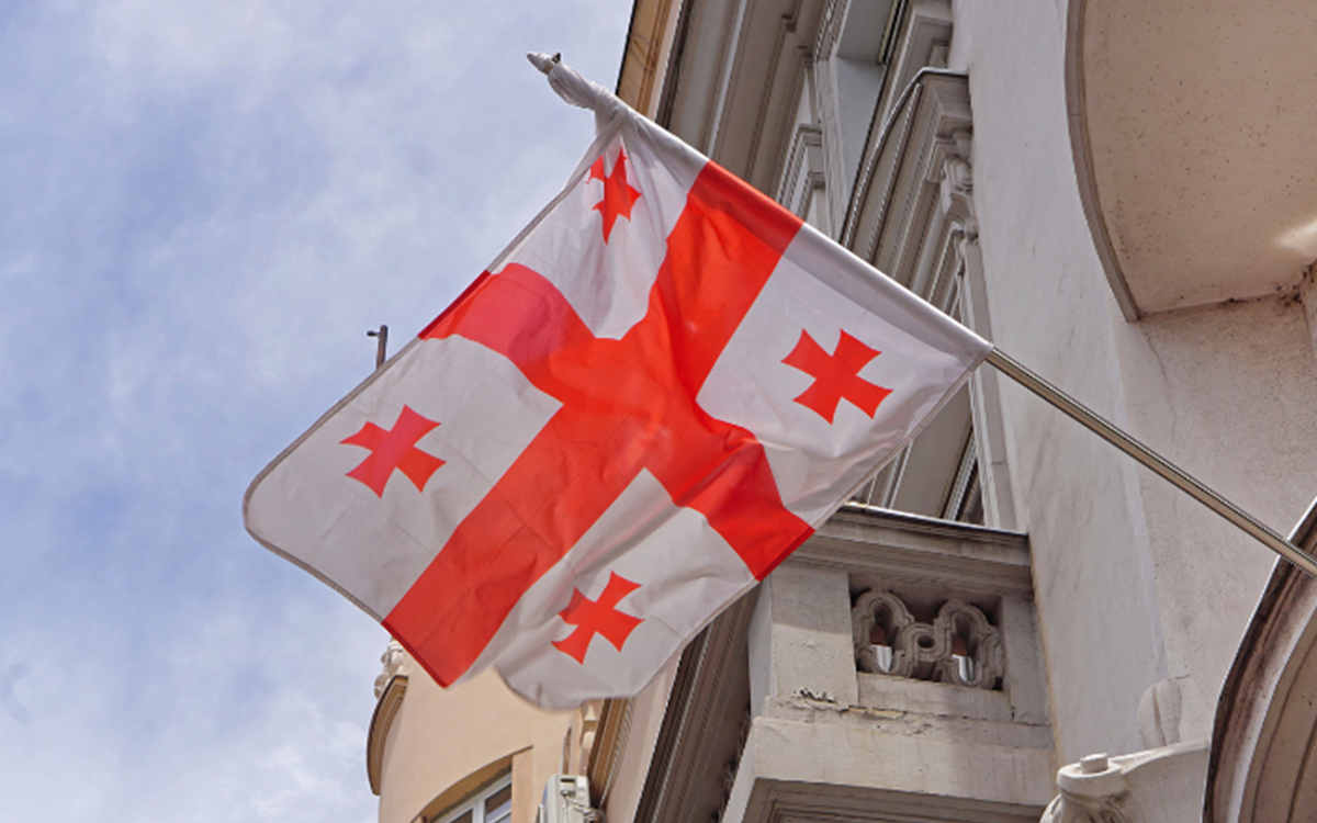 The red and white flag of Georgia flying out of a building from below