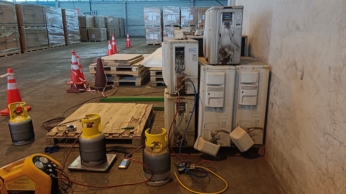 A close-up of grey air conditioning units with grey recovery cylinders with yellow tops in a warehouse