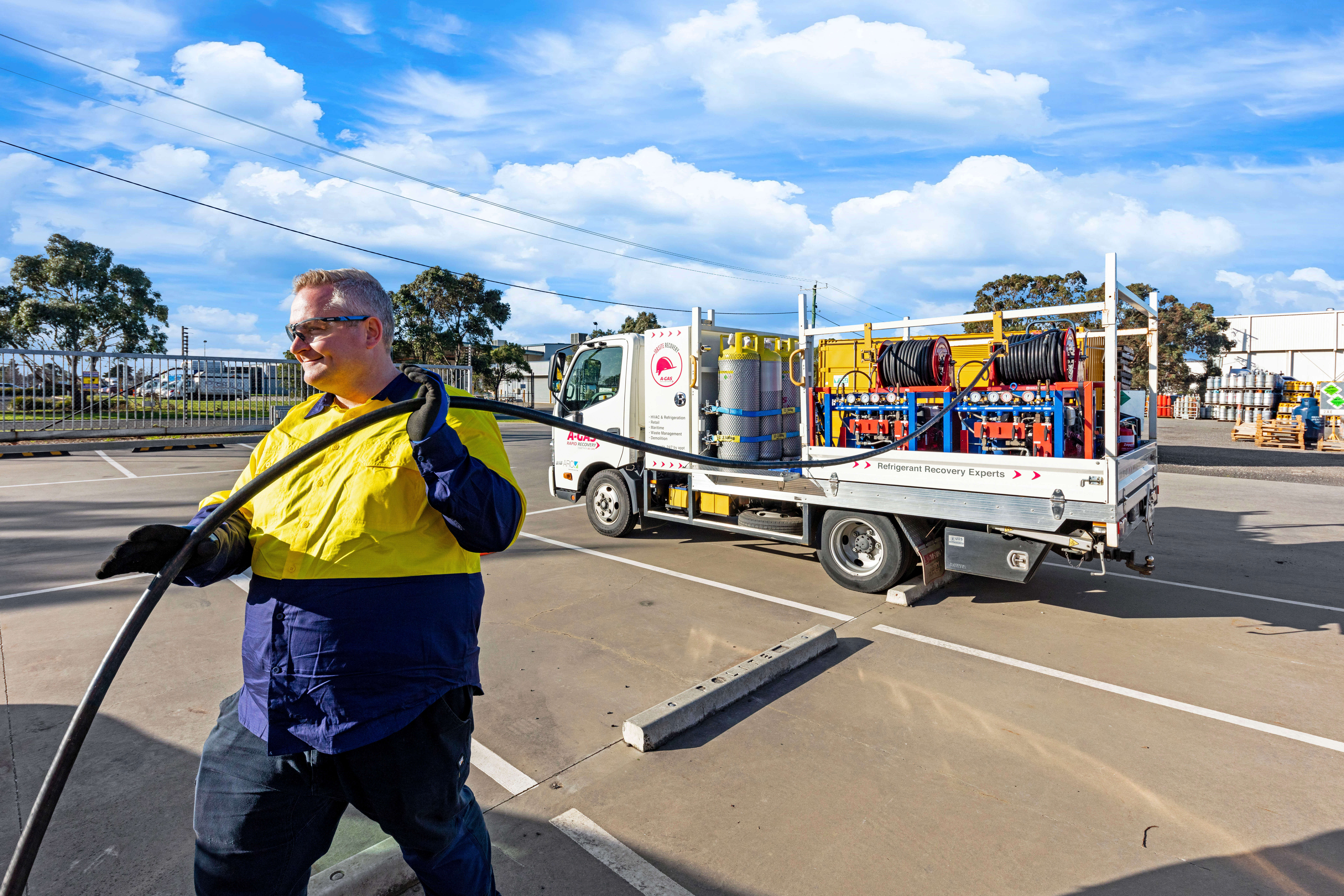 Man smiling while pulling black hose from the back of a white recovery truck 