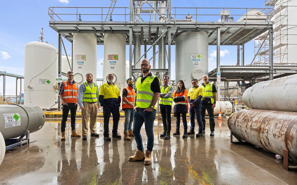 A group of men and women wearing high-vis in front of cylinders and smiling at the camera