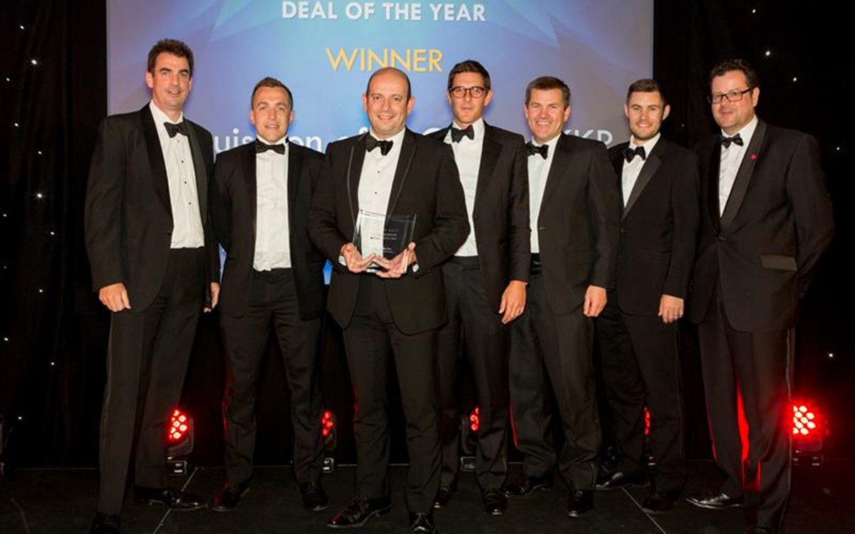 A group of smartly dressed men holding a "Deal of the Year" award