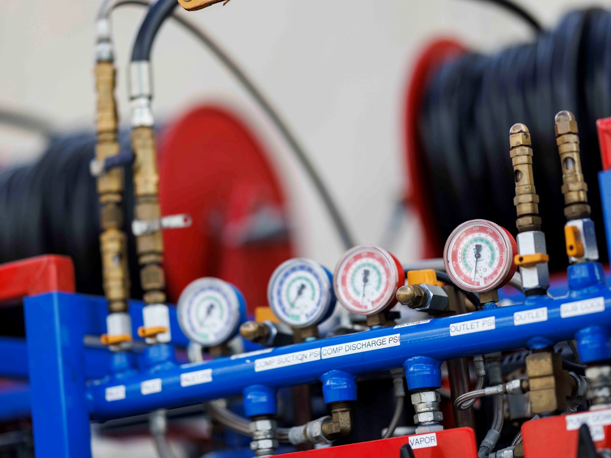 Dials on a piece of blue refrigerant hardware equipment with black hosing attached.