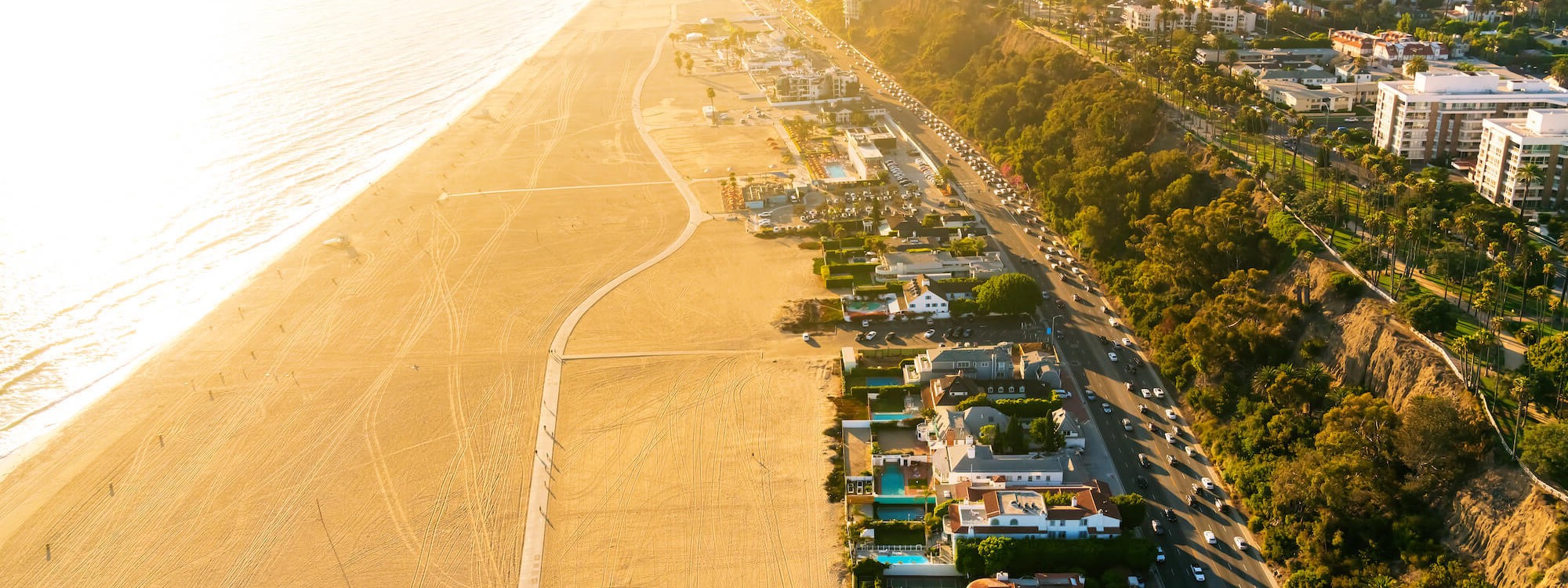 A birds eye view of Santa Monica beach in California. A row of buildings swimming pools stretch along the sandy beach into the distance.