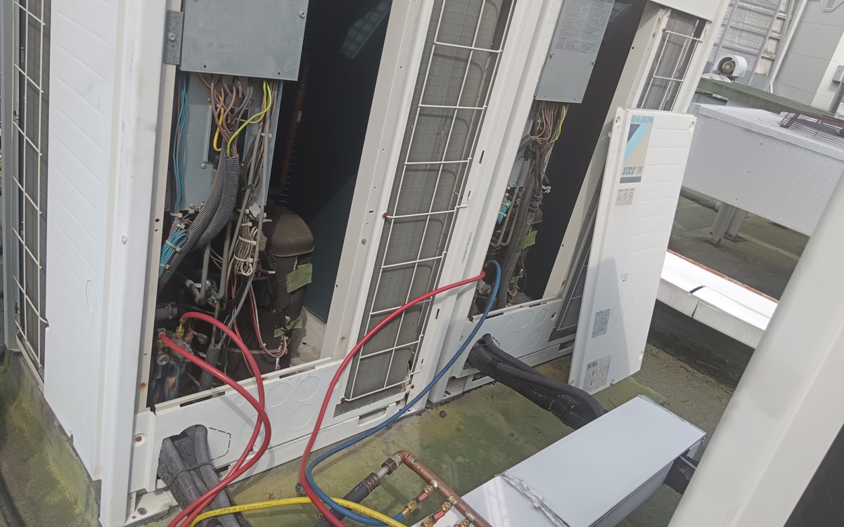 Two large white air conditioning units in a warehouse with hosing coming out of them