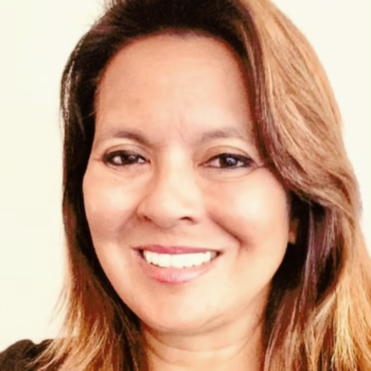 A close-up of a woman smiling against a light beige background