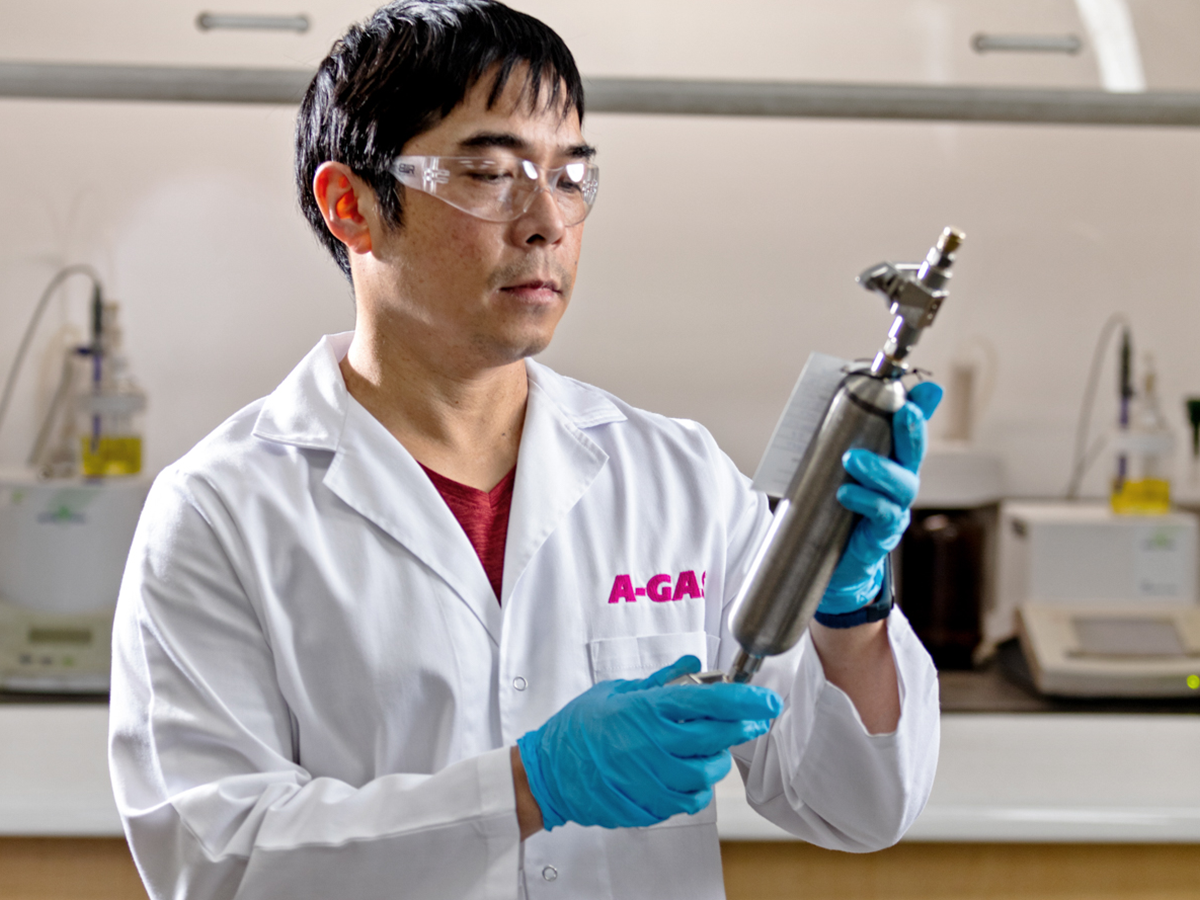 Technician in a white coat holding a silver metal tool in a laboratory