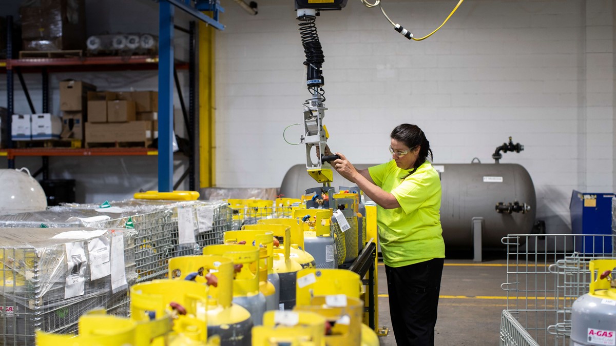 A woman in a warehouse operating a crane above metal baskets full of gas cylinders