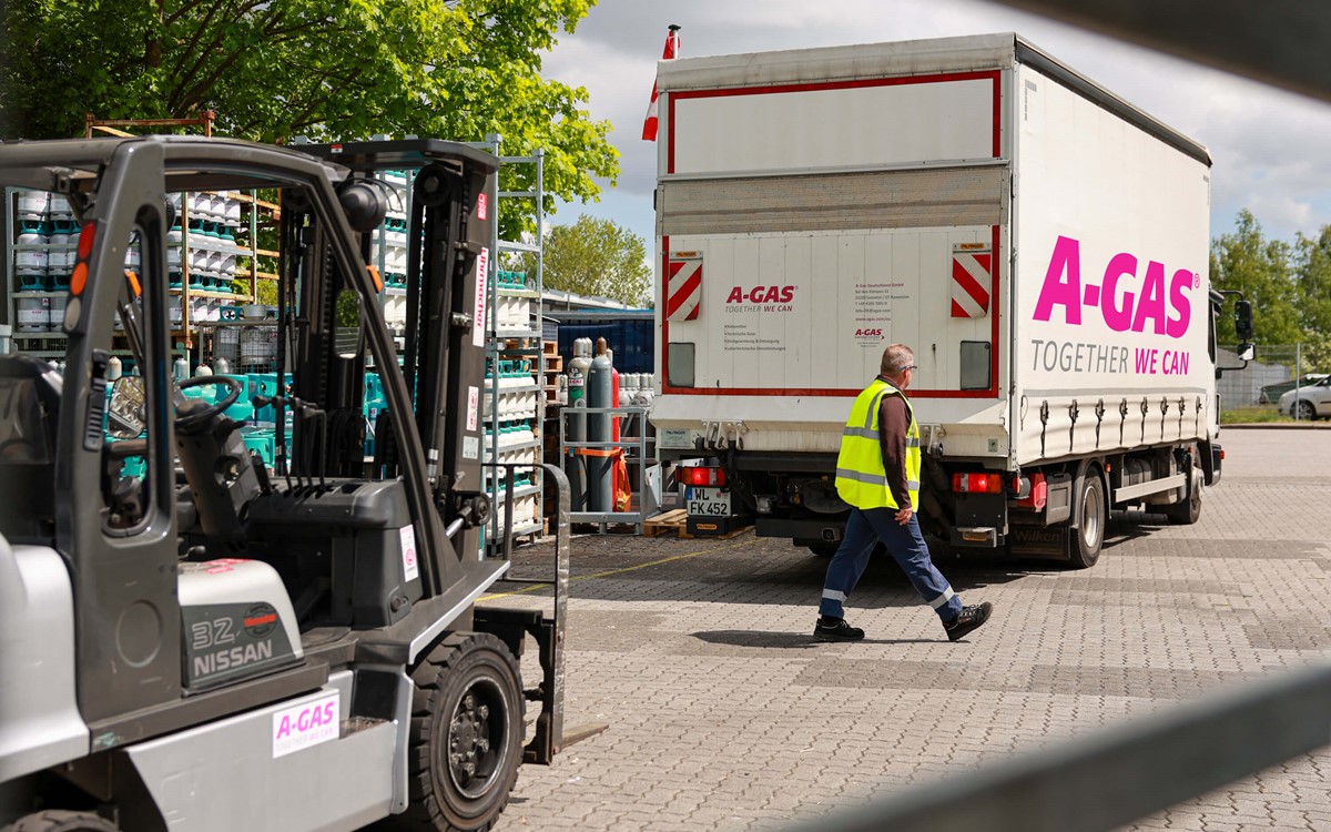 A man in a yellow high-vis jacket walks between a forklift and a white lorry with the pink A-Gas logo