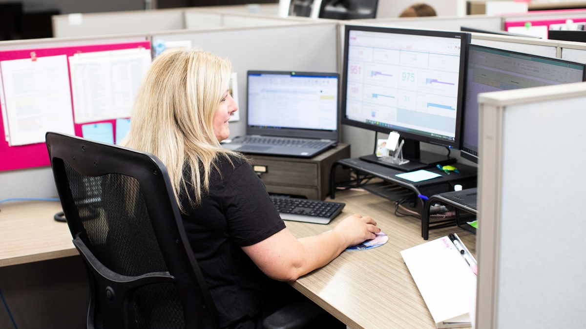 A photo taken from behind of a person sitting in an office pod using their laptop and computer