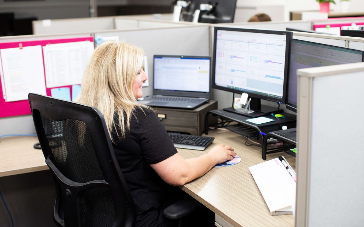 A photo taken from behind of a person sitting in an office pod using their laptop and computer