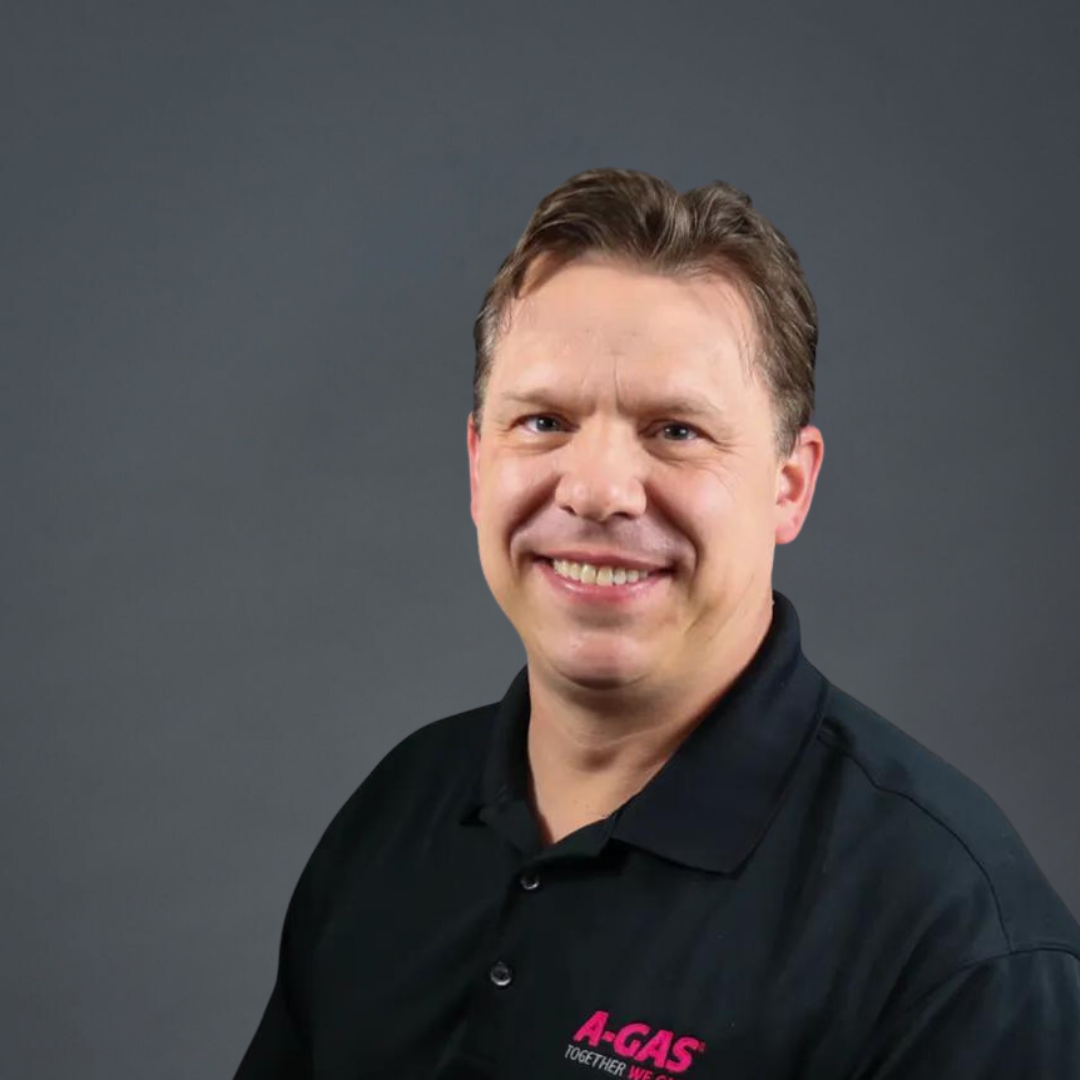 Headshot of a man in blue polo shirt smiling against a grey background 