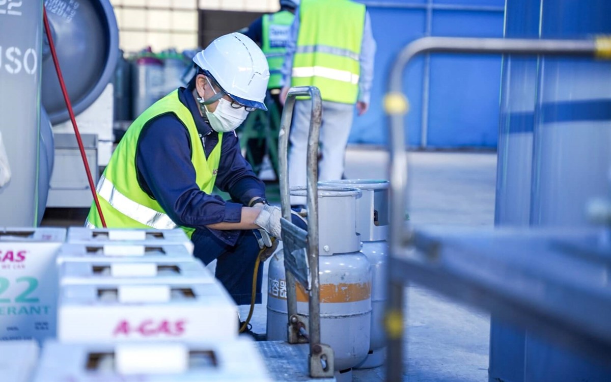 A man in a facemask working with blue cylinders in a warehouse