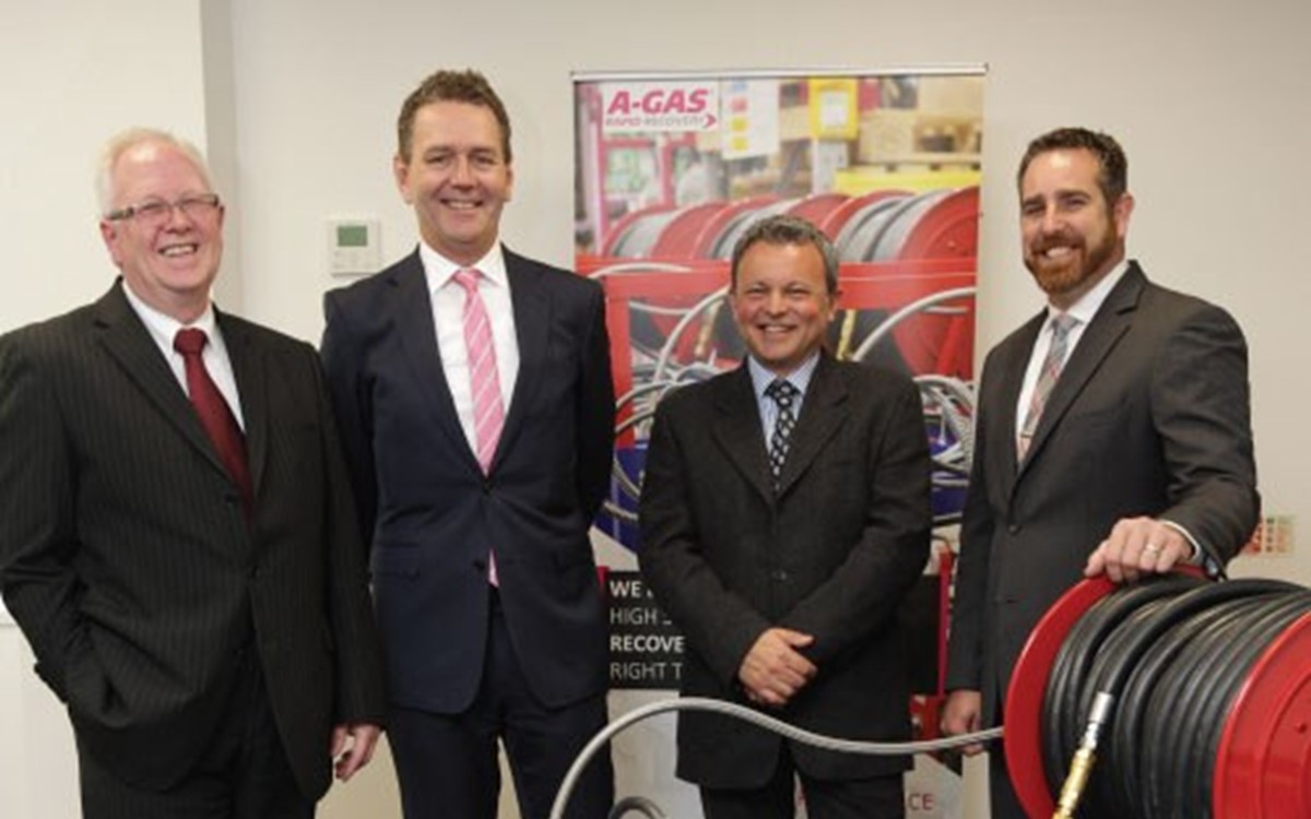 A group of men in suits smiling at the camera behind some recovery equipment in an office