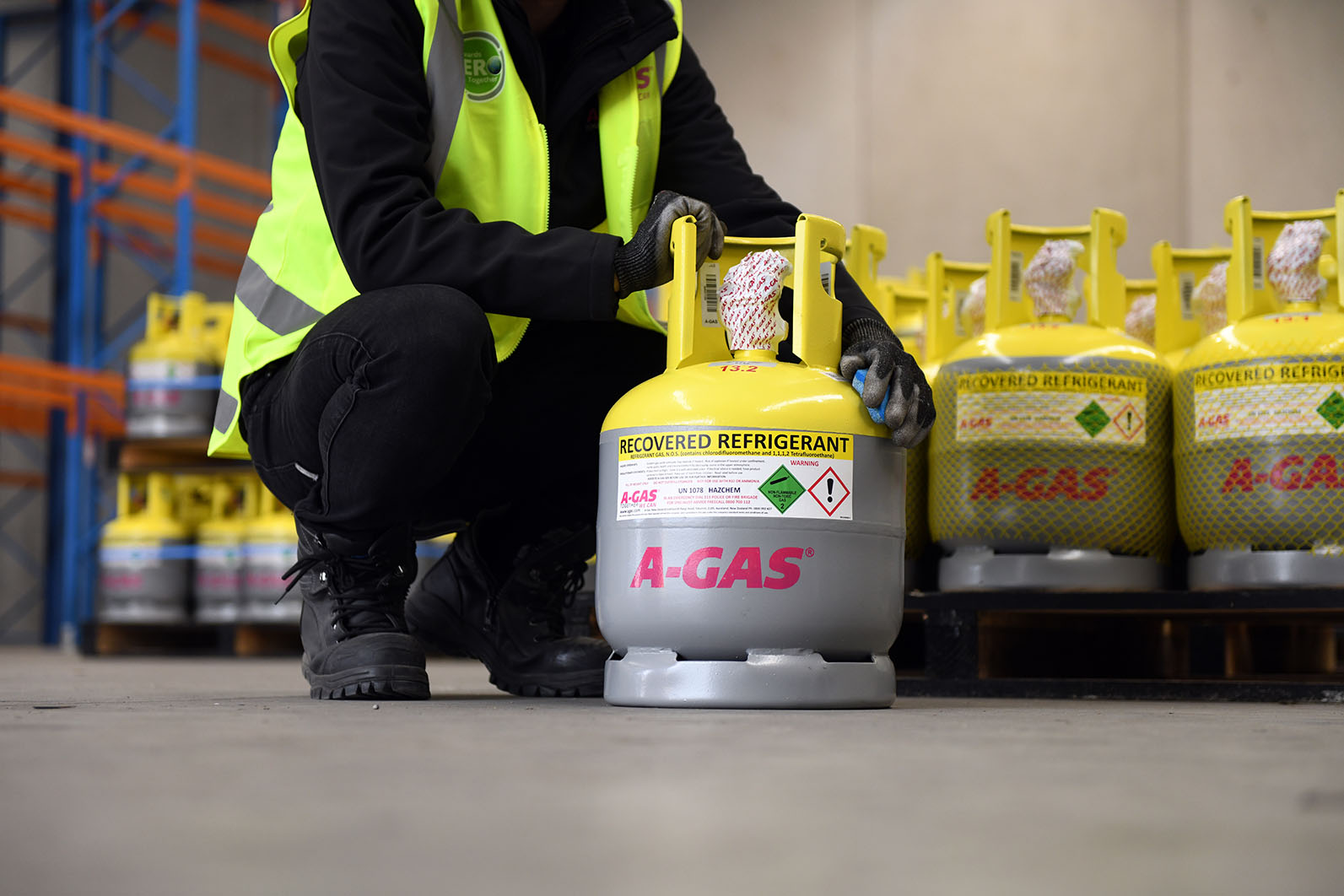 Close-up of a man kneeling down and working on a grey cylinder with a yellow top 