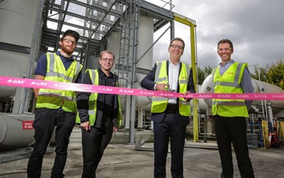 A group of men in yellow high-vis jackets smiling behind a pink ribbon in front of separation towers