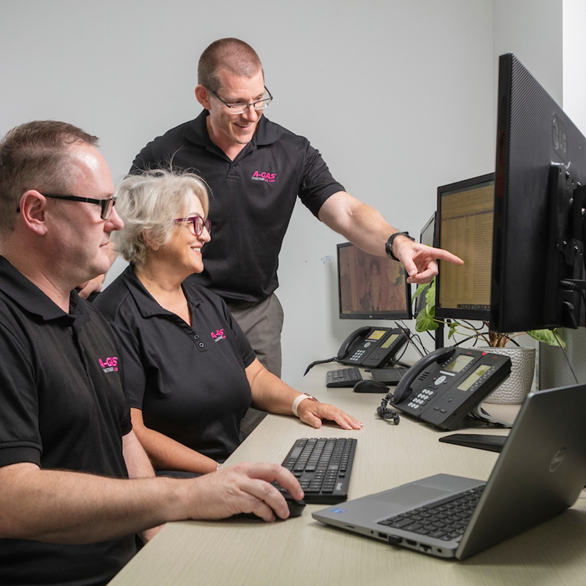 Man pointing at computer screen while smiling next to colleagues in an office