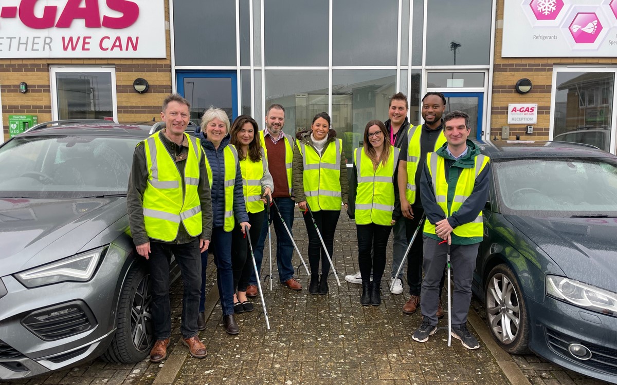 A group of people in yellow high-vis jackets stand outside an office and smile at the camera