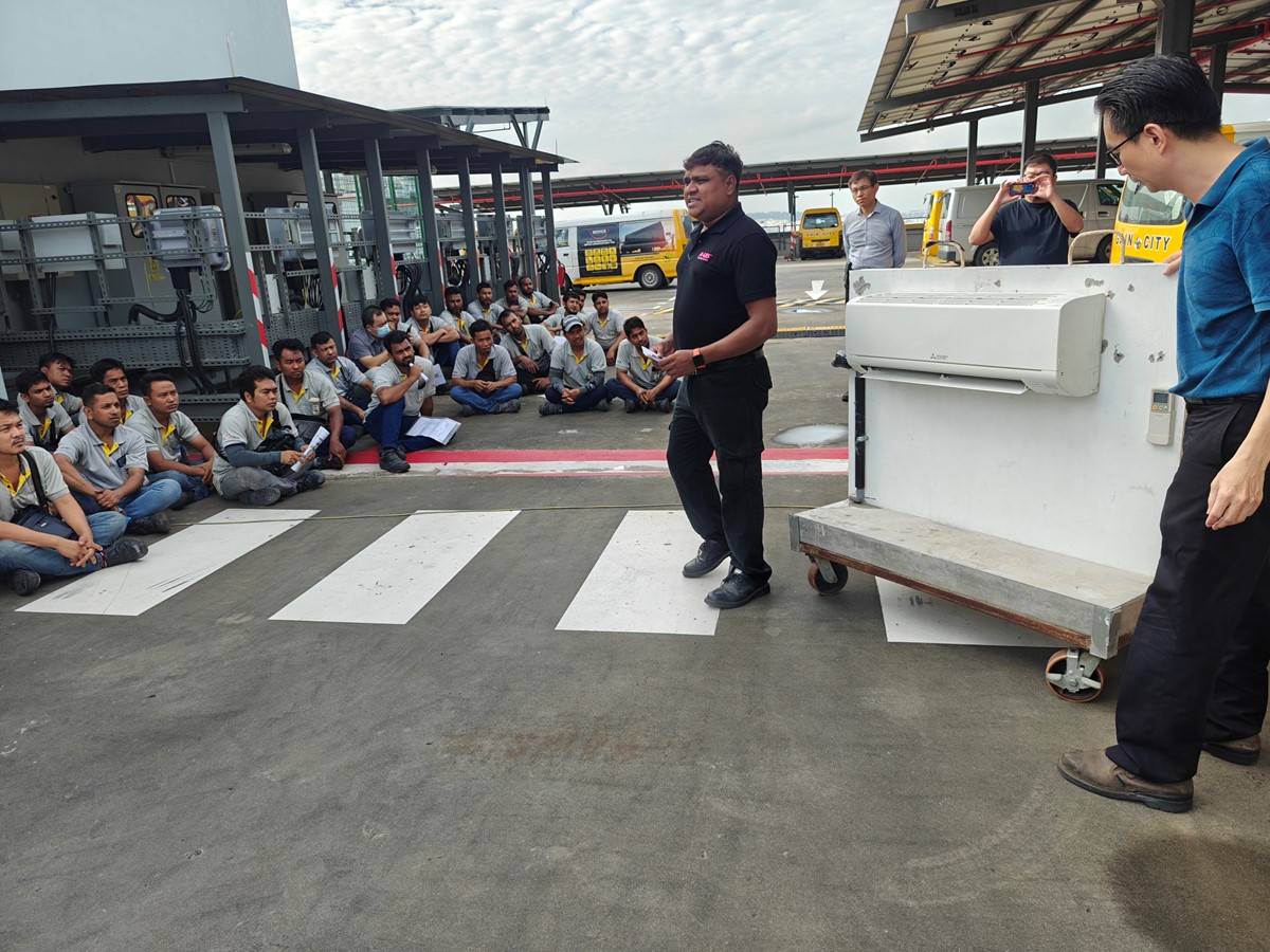 A man speaks to a group of people sitting down on-site