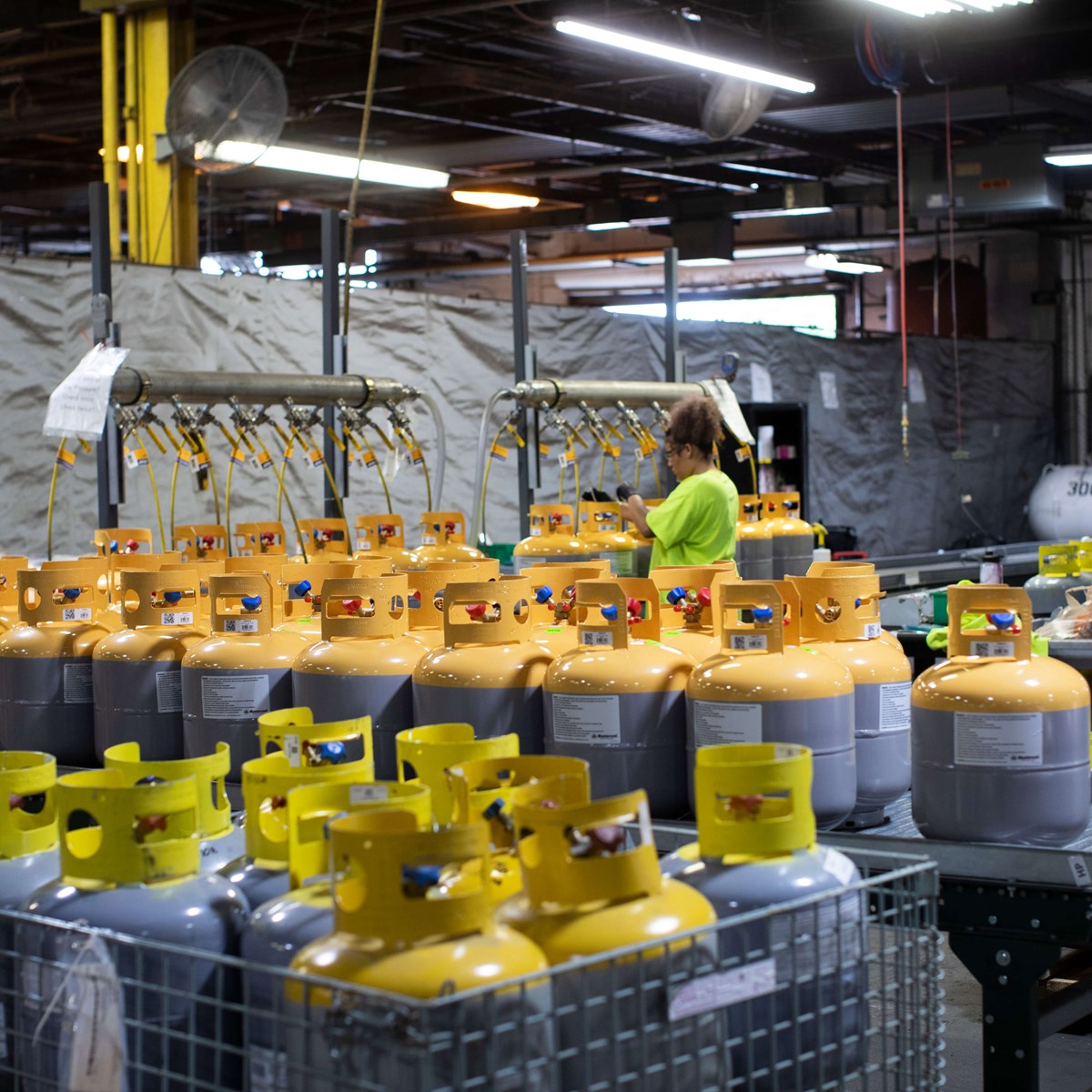 A wide shot of lots of yellow and grey cylinders with a woman working in the warehouse with the cylinders