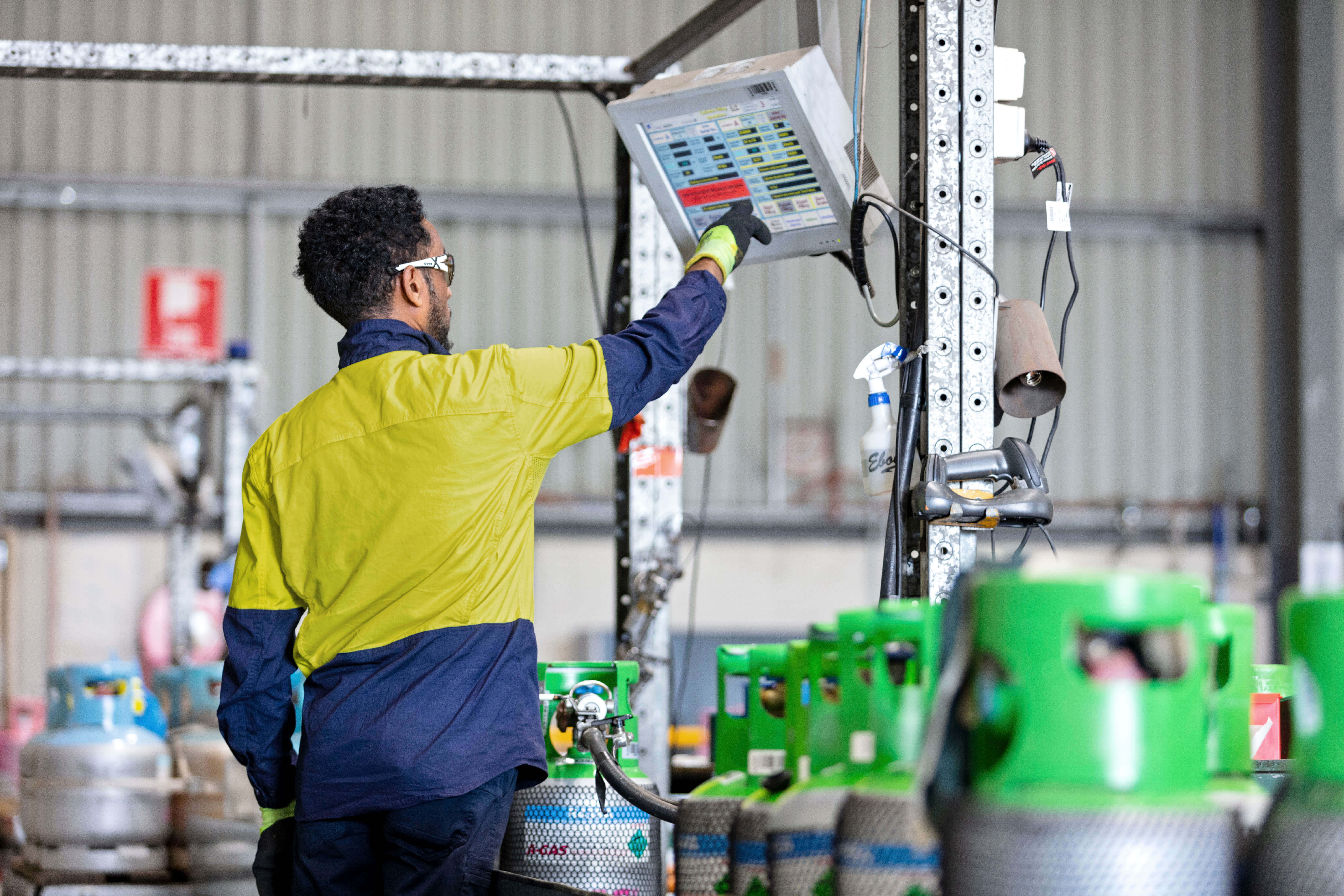 Technician in high-vis jacket filling a green-topped gas cylinder via a hose 