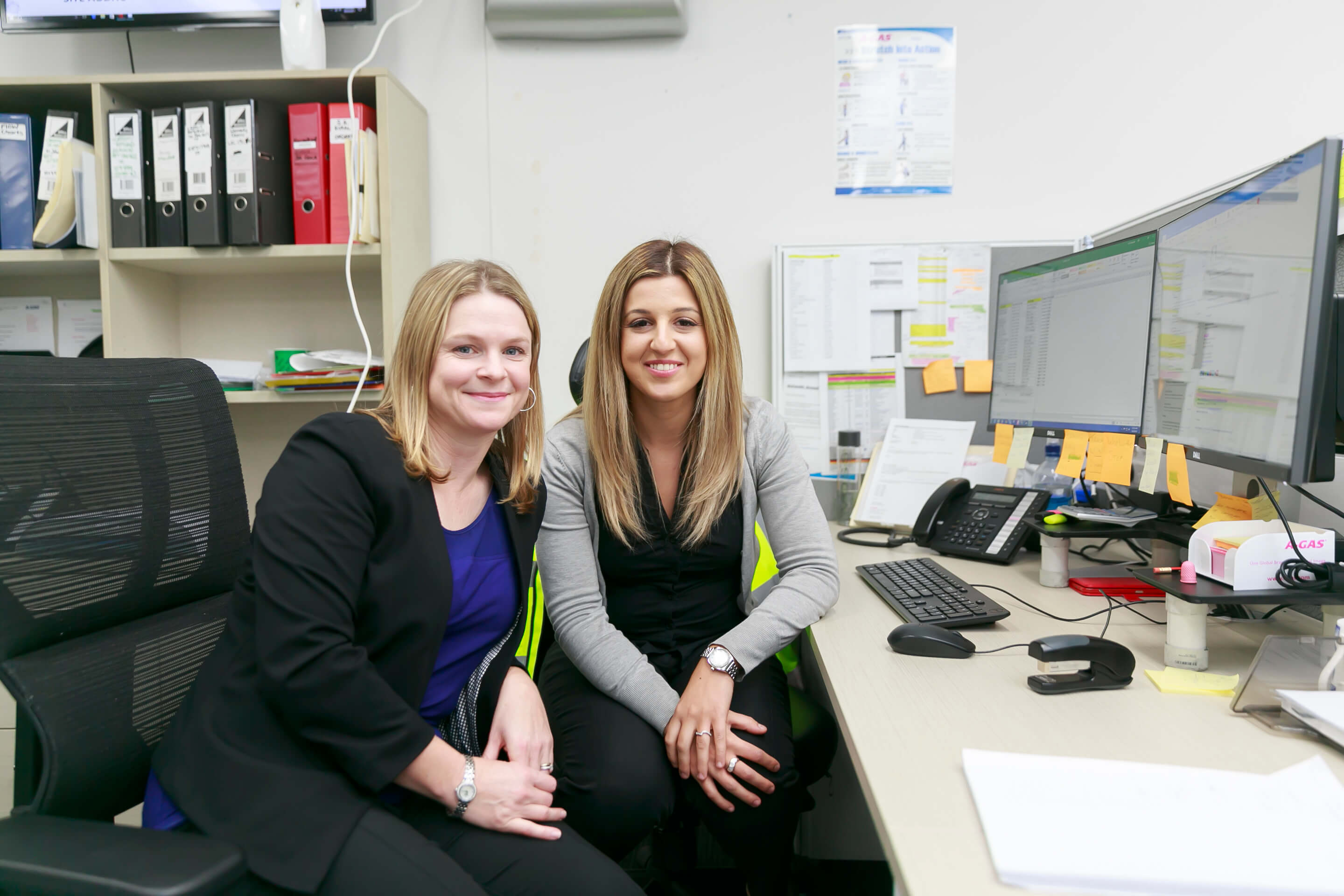 Two women sat in their office smiling at the camera