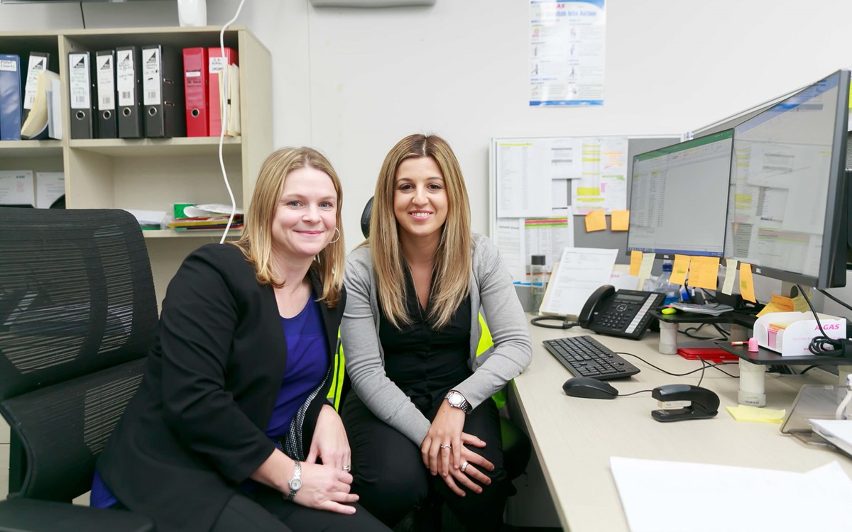Two women sat in their office smiling at the camera