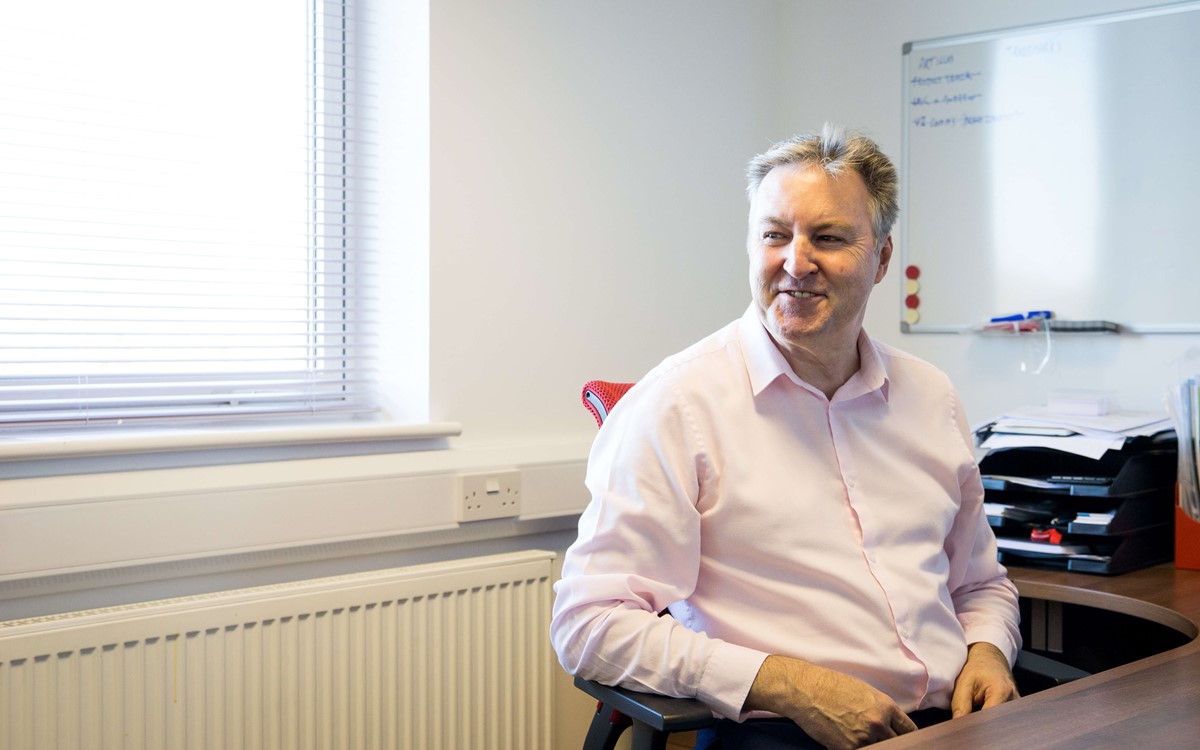 A man sat at his desk looking to the left smiling