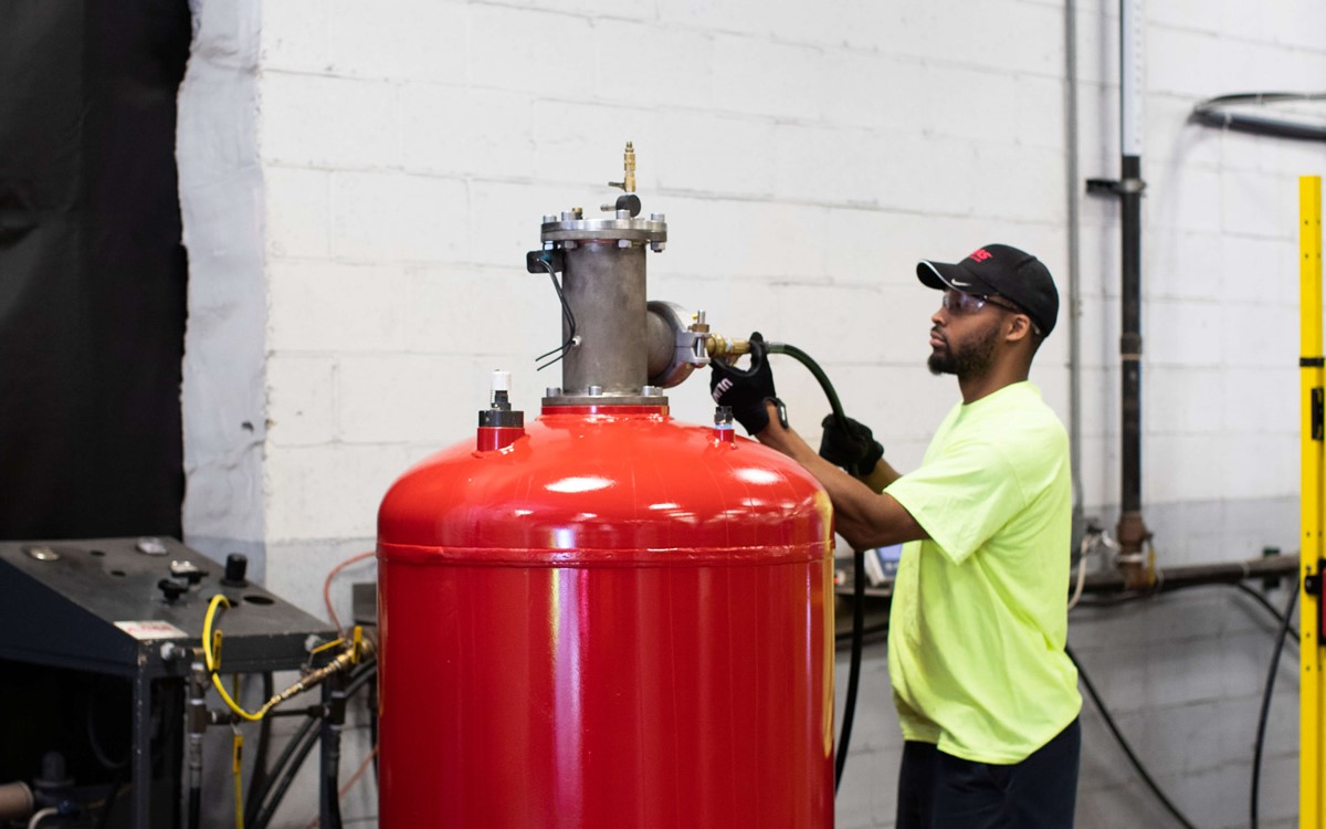 A person working with a large red half ton cylinder, the cylinder is taller than him