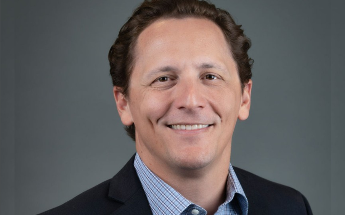A headshot of a smartly dressed man smiling against a grey background