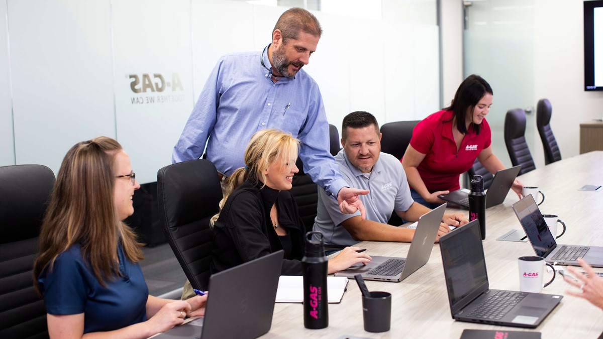 Men and women sat in the boardroom looking at a laptop, there is one man standing up pointing at the screen