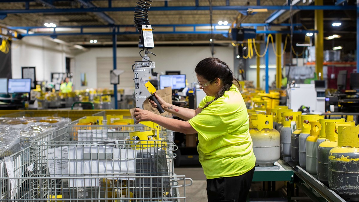 A woman in a warehouse operating a crane above metal baskets full of gas cylinders