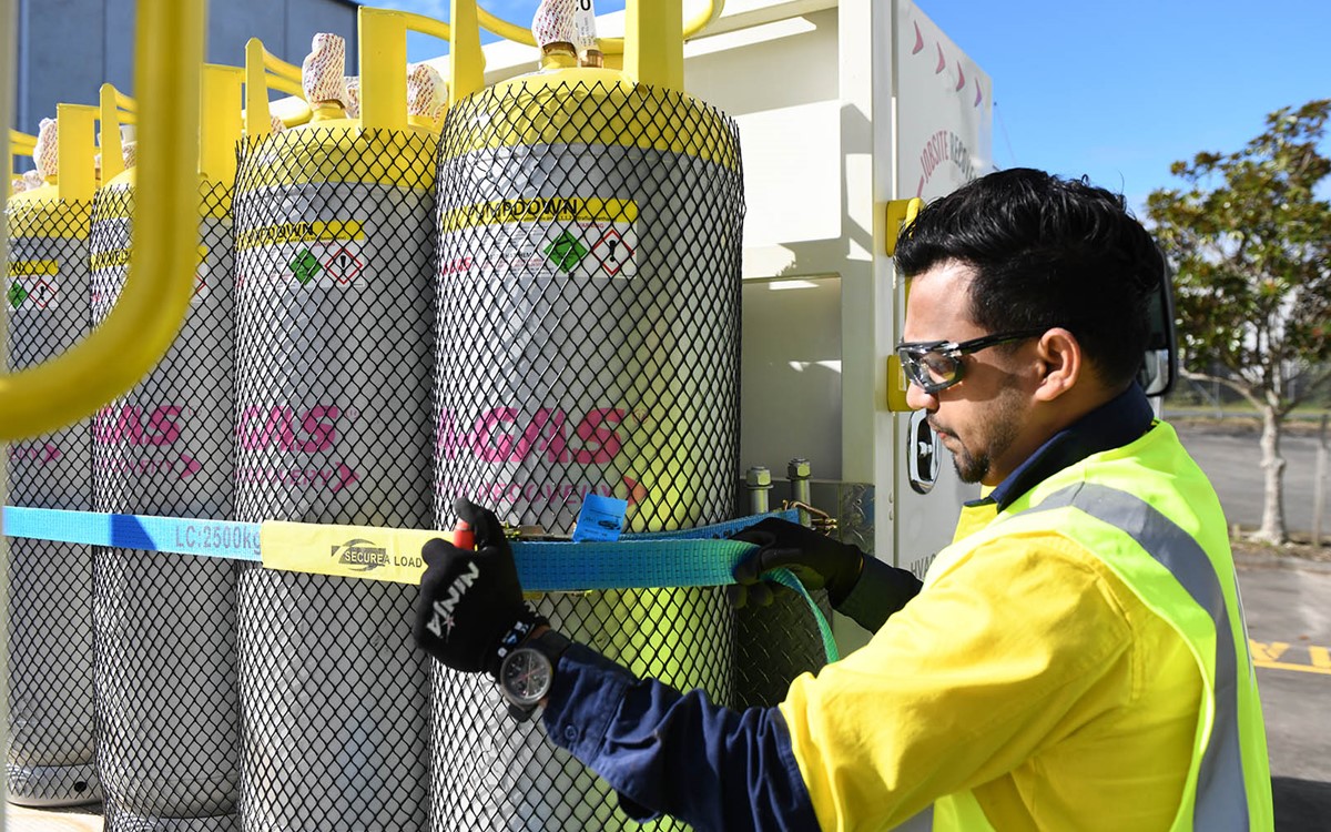 An operator securing large grey cylinders on the back of a white A-Gas truck