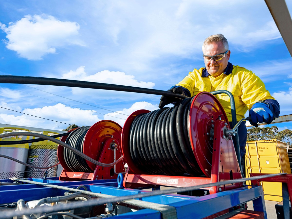 Man working with black hose on the back of a recovery truck
