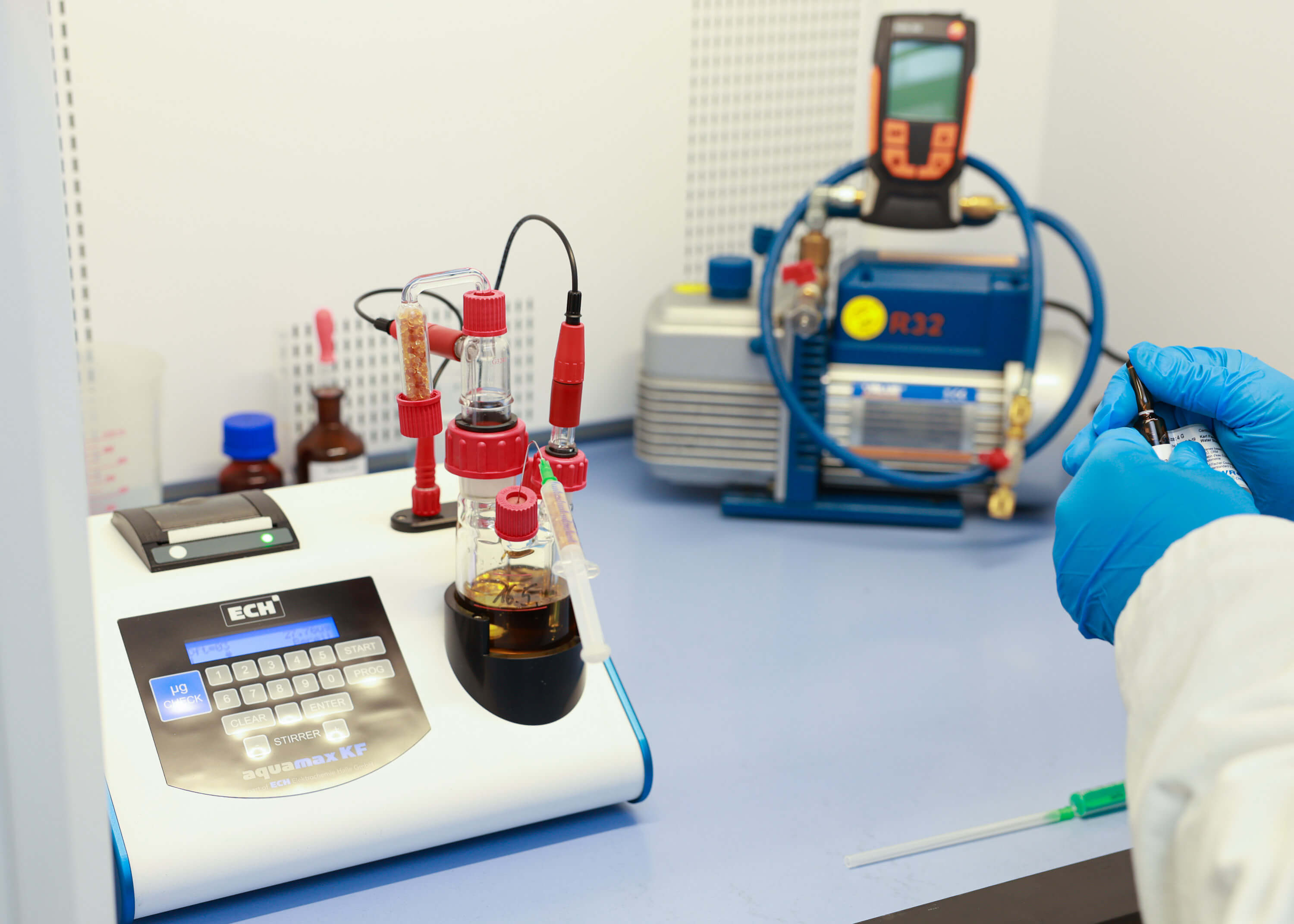 A person wearing blue gloves and a white coat works with laboratory equipment 