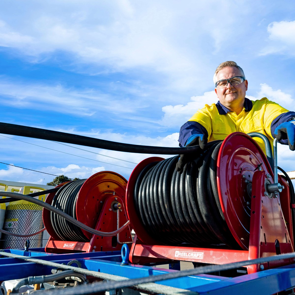Man working with black hose on the back of a recovery truck while smiling at the camera