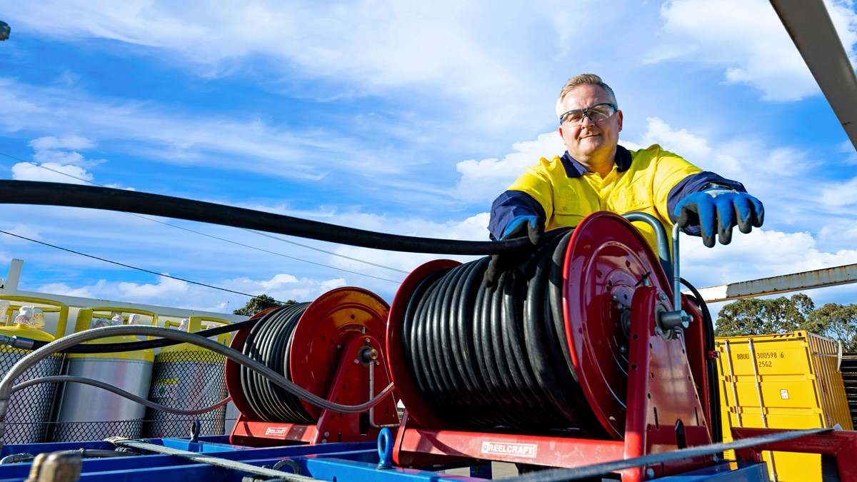 Man working with black hose on the back of a recovery truck while smiling at the camera