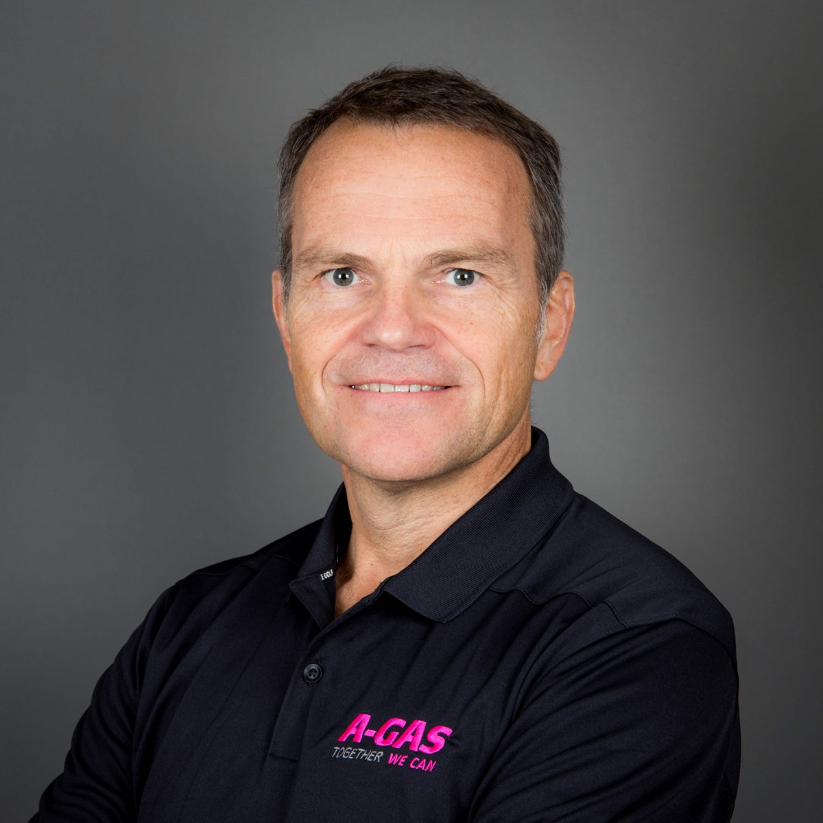 A headshot of a man in a black polo with a grey background