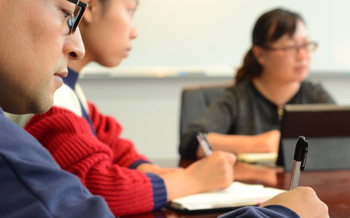 Close up of a man in a meeting, there are other people visible in the background