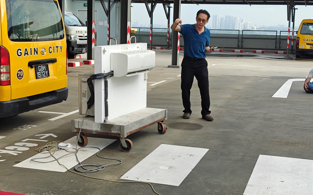 A man talks while demonstrating with a white air conditioning system outside