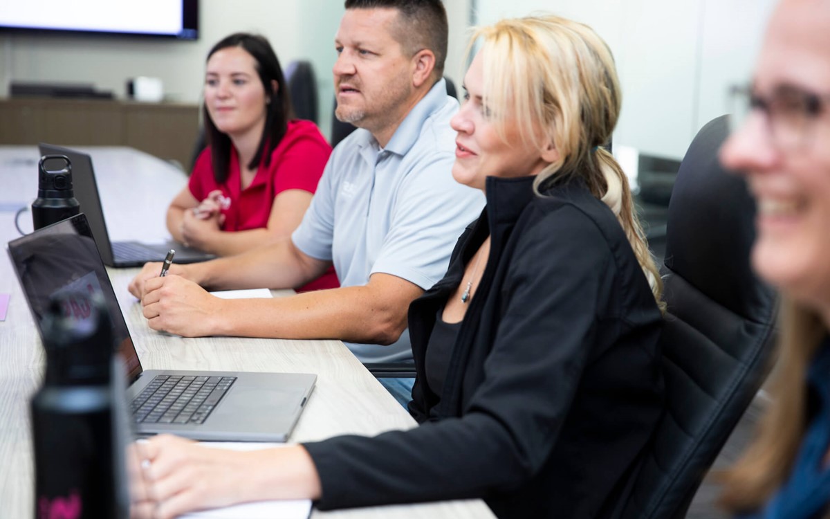 A group of men and women sat around a board room table, they are laughing