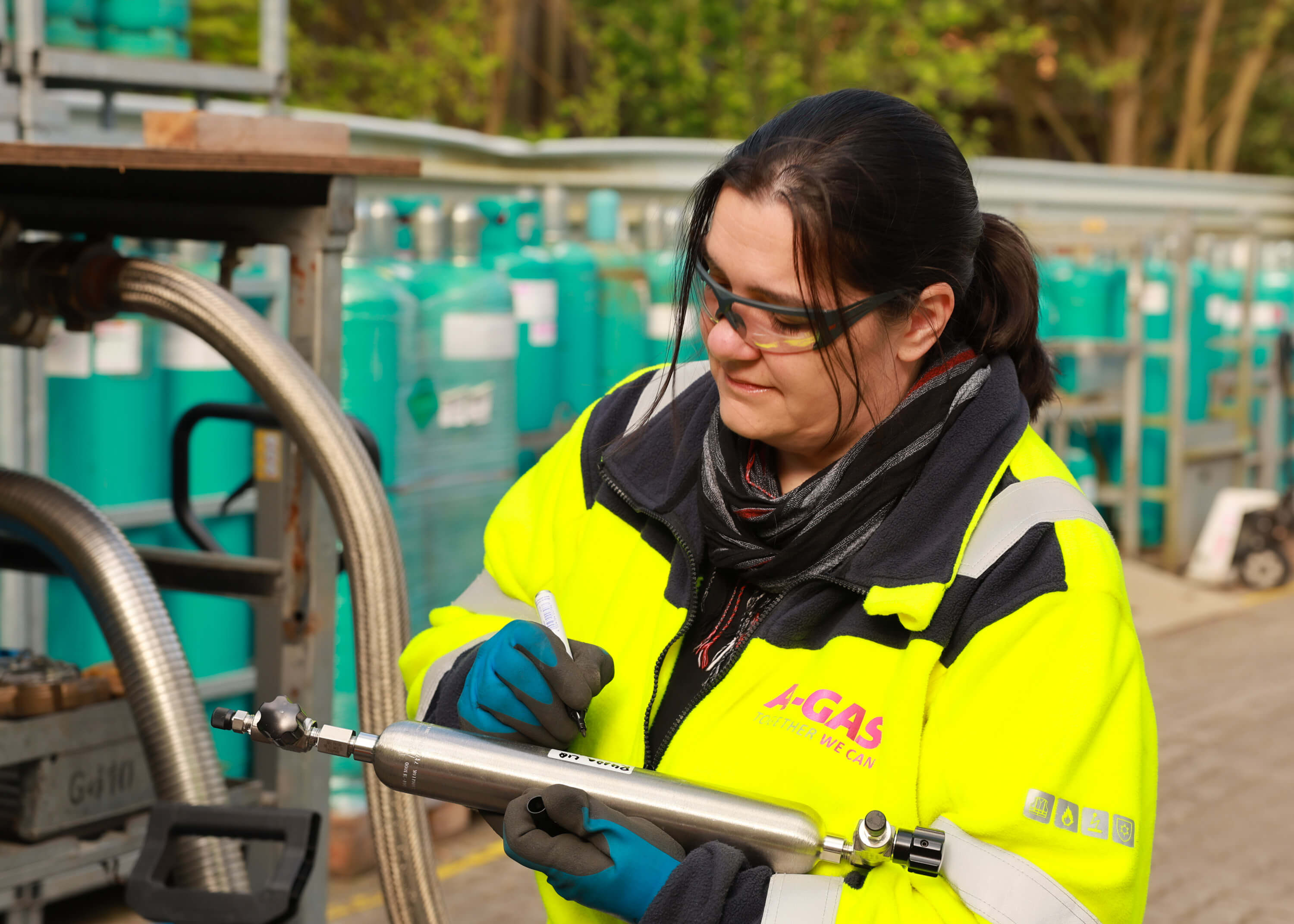 A woman in a yellow high-vis jacket writing on a metal piece of equipment 